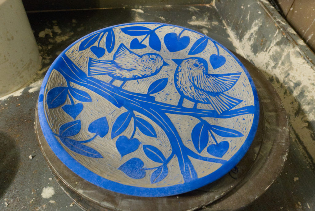 unfired pottery plate with blue decorations of 2 birds on a tree branch