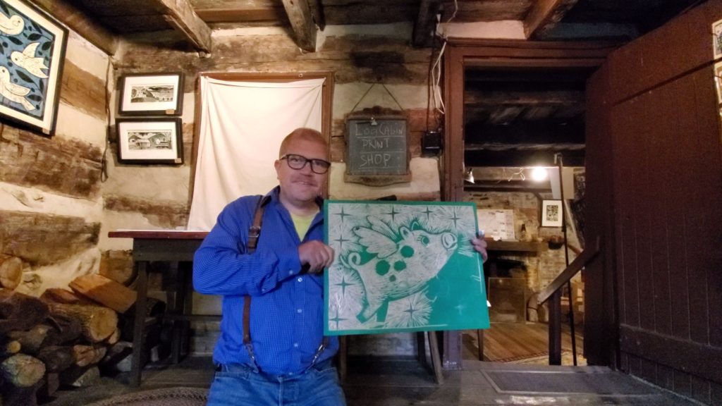 artist ken swinson holding woodcut work in process of a flying pig at the log cabin print shop in old washington kentucky