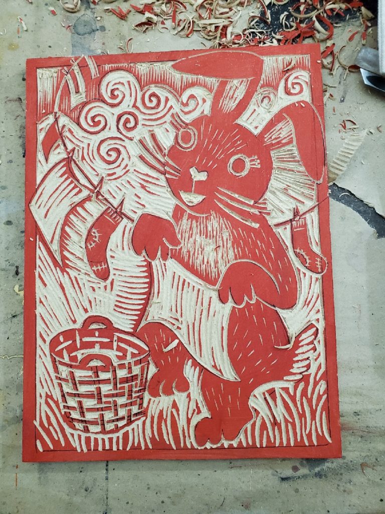 a carved woodcut of a bunny rabbit hanging laundry on the line