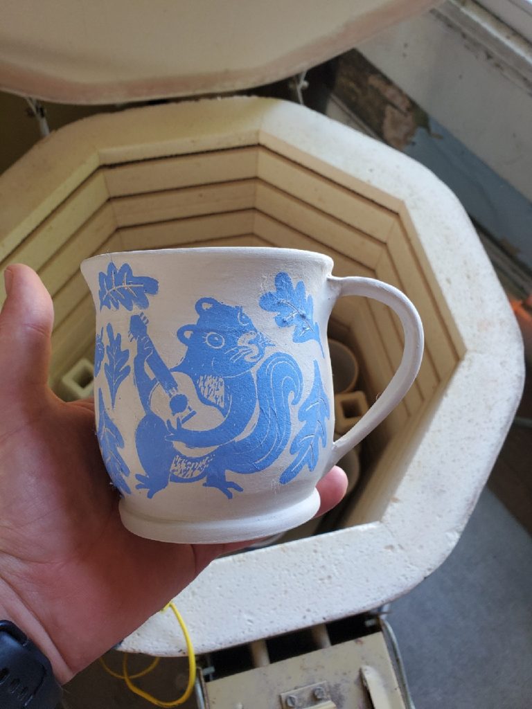 holding a greenware mug with decal of squirrel playing guitar