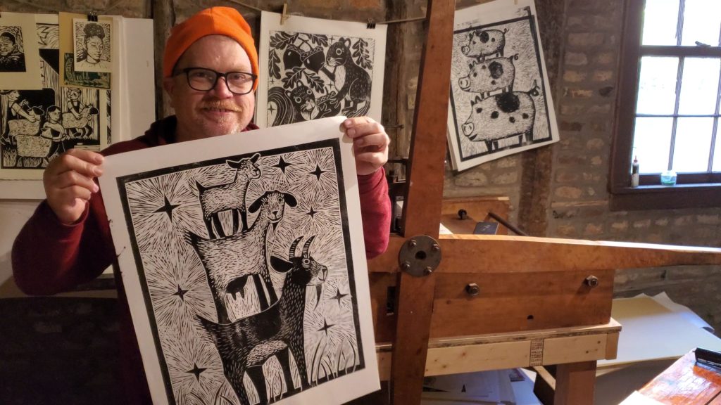 artist holding test proof of 3 goat woodcut