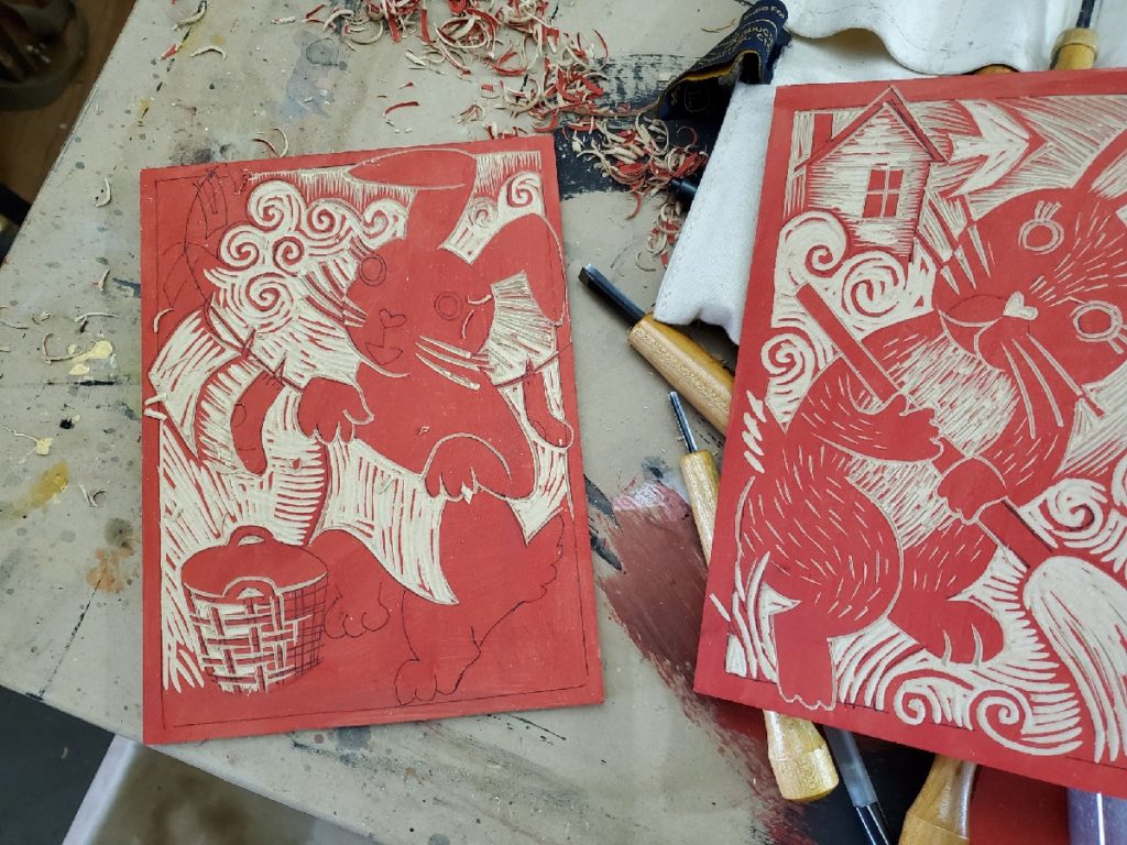 2 woodcut works in progress a bunny sweeping another hanging laundry on the line