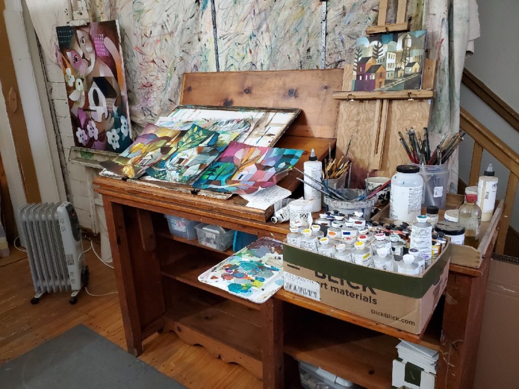 desk covered with art supplies and paintings