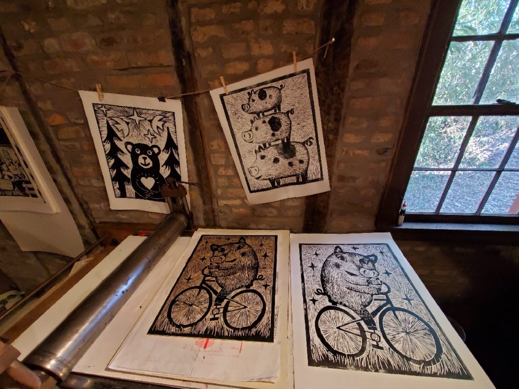 a test proof of pig on bike woodcut inside a log cabin