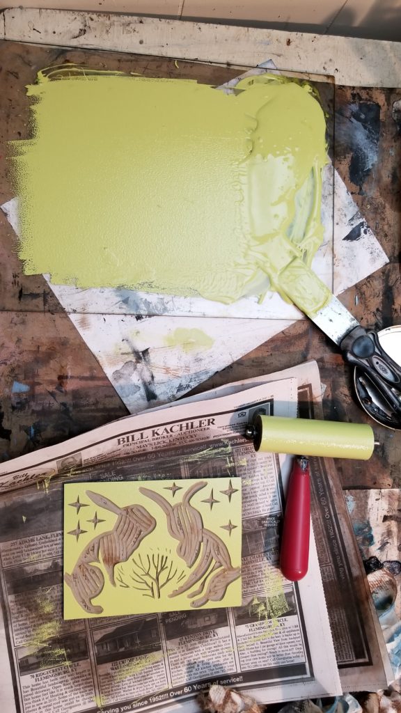 busy printmaking table with green ink brayer and linocut