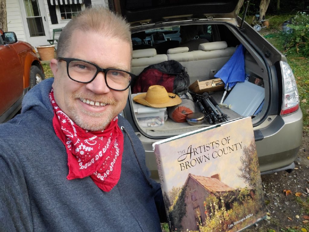 Artist with car packed with art supplies, holding a book of brown county artists