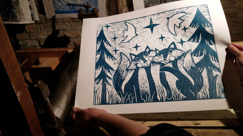 artist holding large woodcut of two foxes in the woods under a star