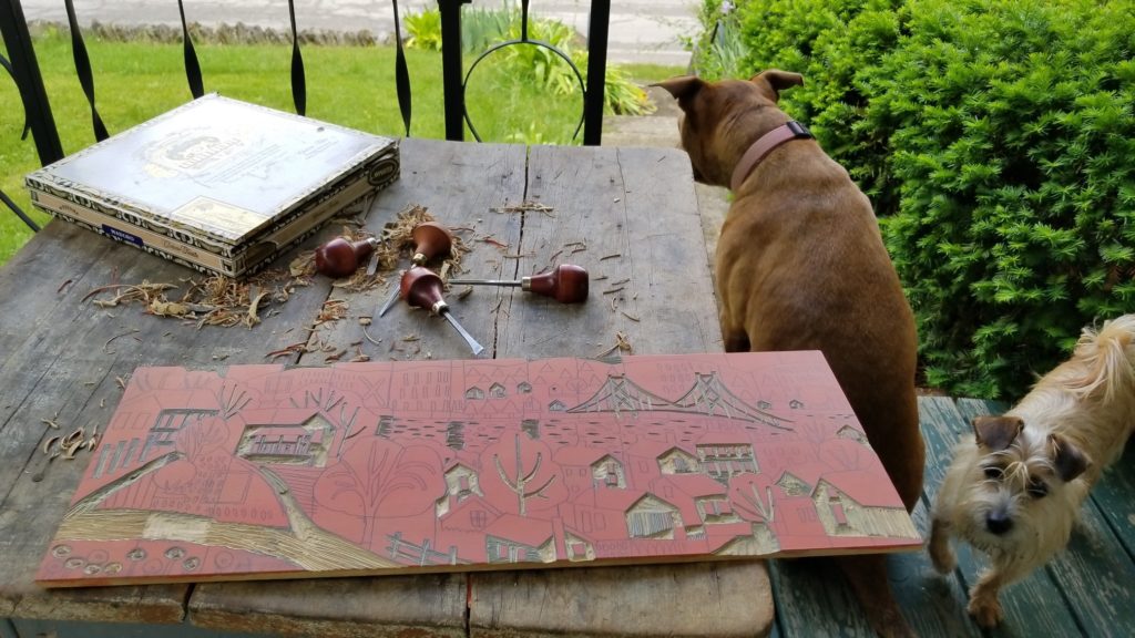 on porch carving a reduction woodcut with dogs watching