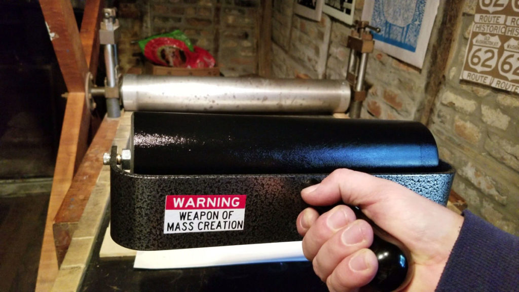 traditional printmaking brayer with warning sticker 'weapon of mass creation'