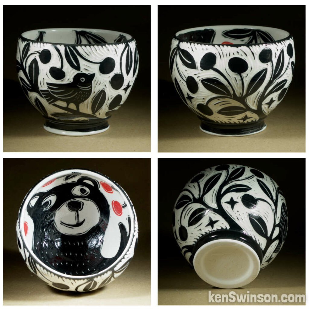 A wheel thrown porcelain bowl with black and white sgraffito design of birds on a cherry tree on the exterior. the interior has a bear picking red cherries