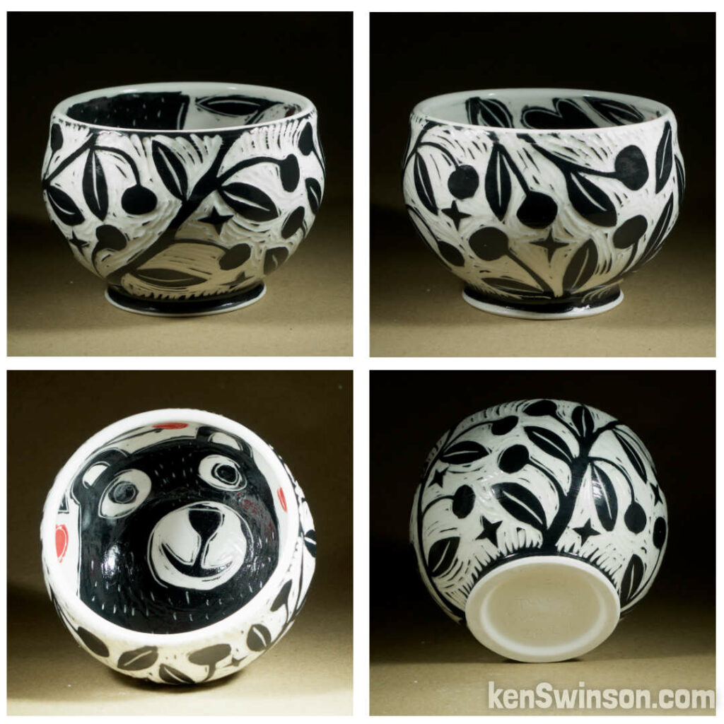 A wheel thrown porcelain bowl made by Kentucky artist, ken swinson-the bowl is decorated with black and white sgraffito design of cherries on the exterior. the interior has a bear and red cherries