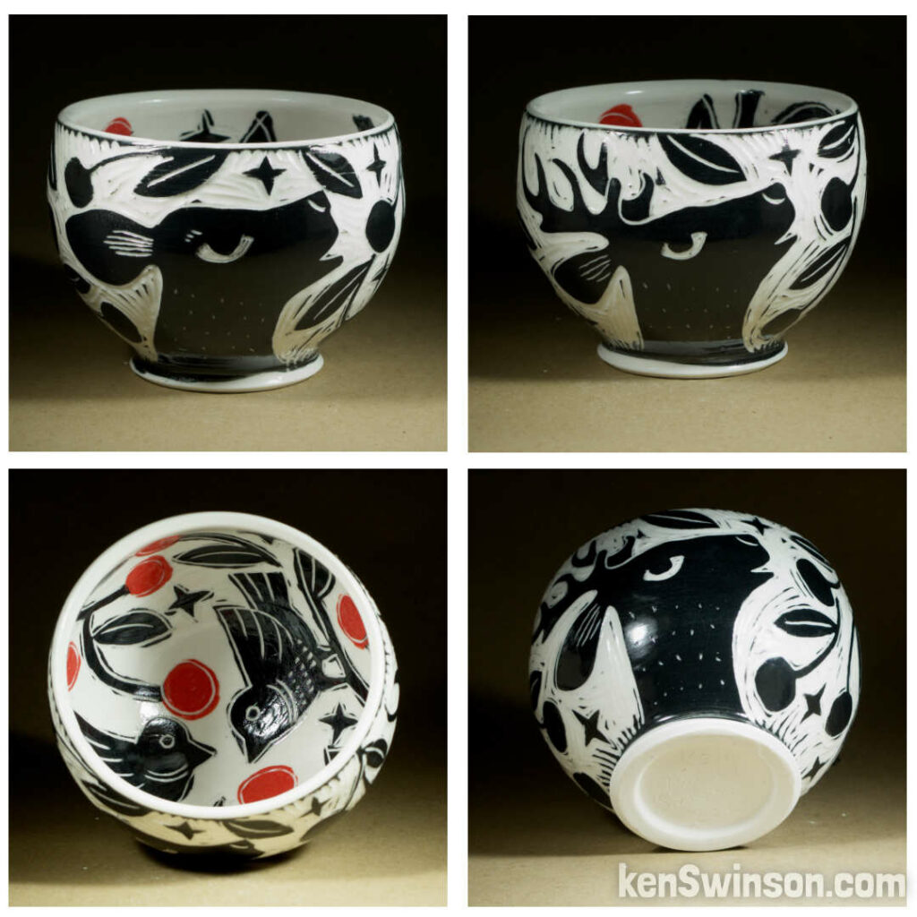 A wheel thrown porcelain bowl made by Kentucky artist, ken swinson-the bowl is decorated with black and white sgraffito design of deer eating cherries from a cherry tree on the exterior. the interior has a birds and red cherries