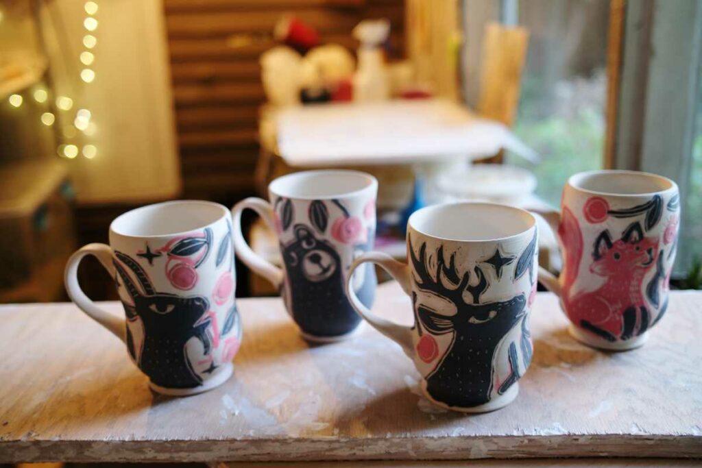 4 work in progress cups: a goat, bear, deer and fox eating cherries from a tree