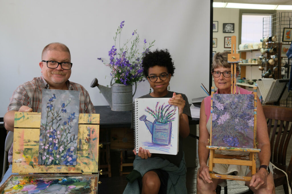 3 artists holding paintings of larkspur