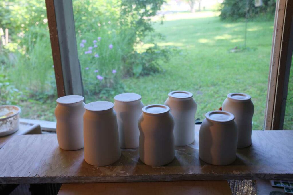 a group of work in progress porcelain pottery cups. The forms are upside down, four are trimmed, three are untrimmed