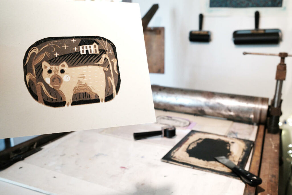 photo of a reduction linocut pig print with a press in the backgroud